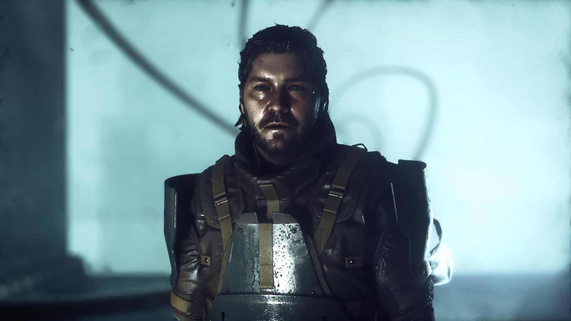 A white man with a beard and long hair looks at the camera with body armor on